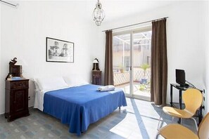 Ein Zimmer mit einem Bett, einem Schreibtisch, einem Sessel, einem Fernseher und einem fensterbepflanzten Fenster.
