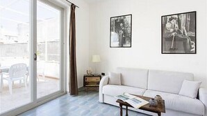 Een woonkamer met een witte bank, een bijzettafeltje en twee ingelijste foto's aan de muur.