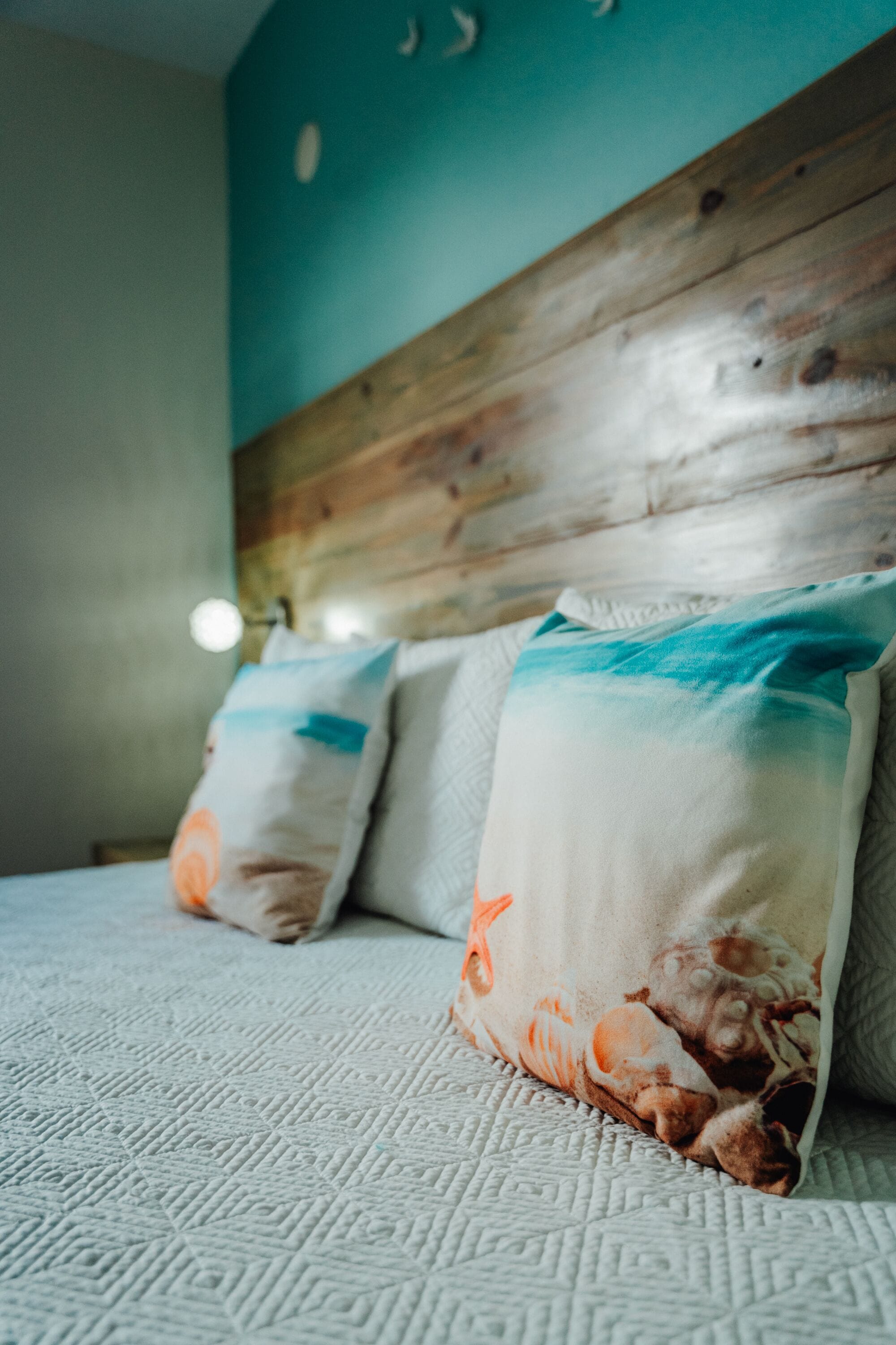 Ein Bett mit weißer, strukturierter Bettdecke und zwei Kissen mit maritimen Motiven.