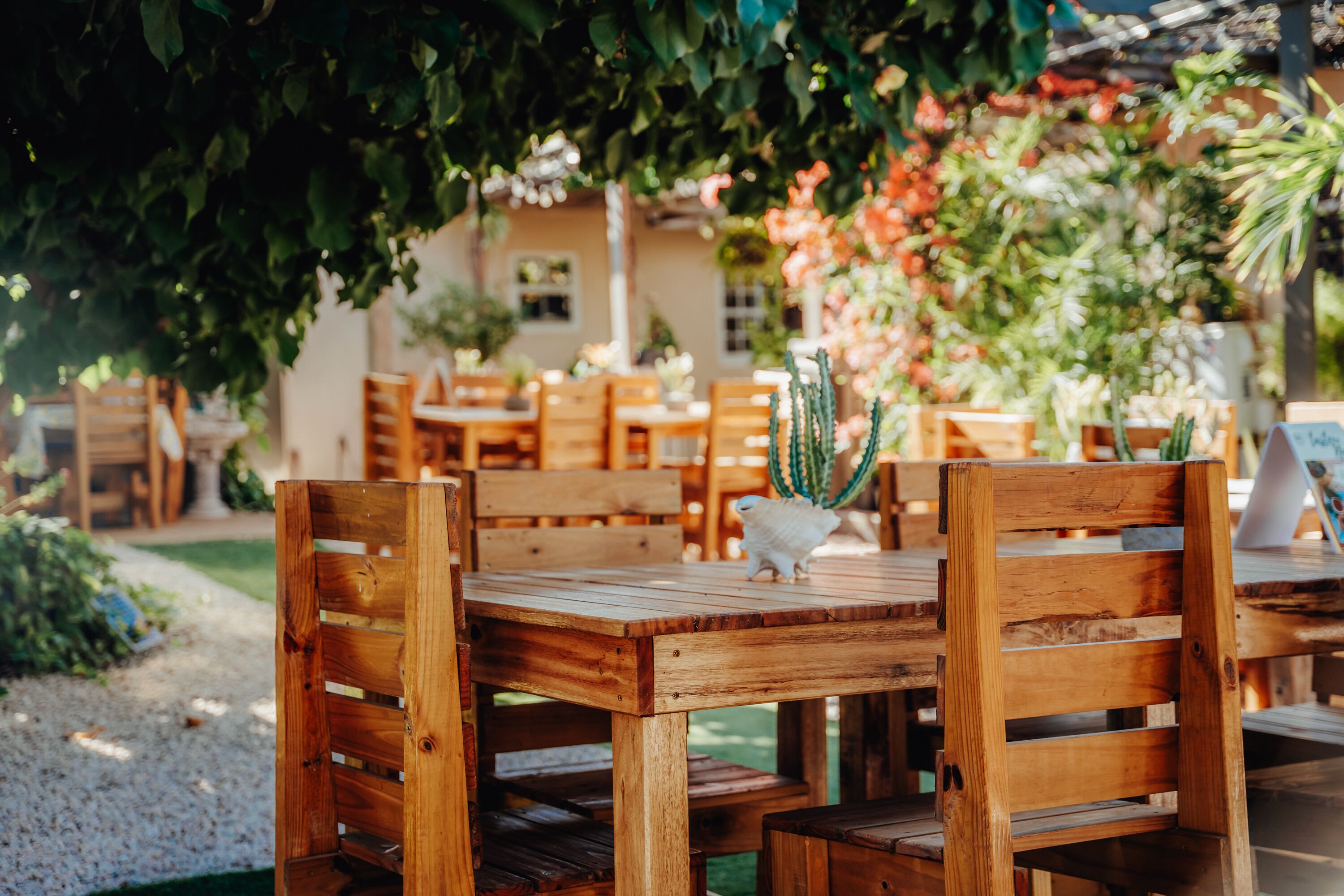 A wooden outdoor dining area with tables and chairs, surrounded by greenery and plants.