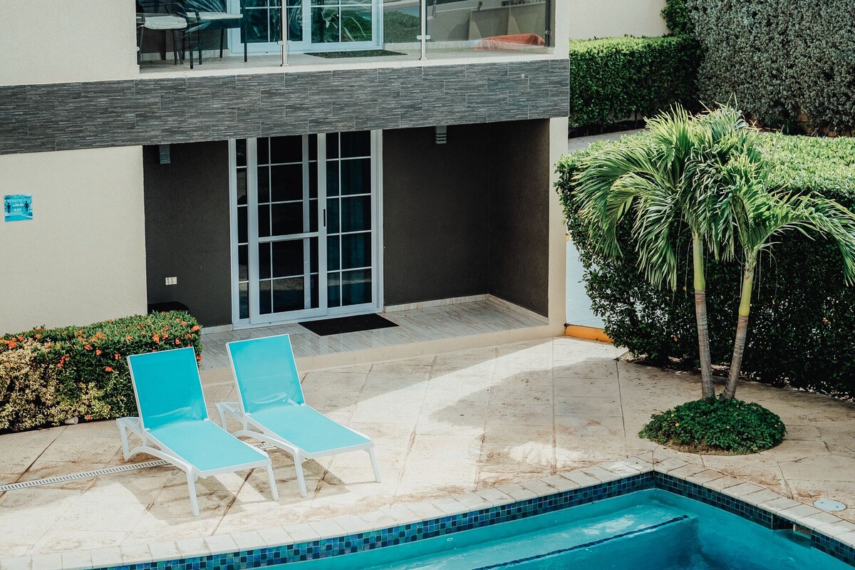 A modern two-story building with a swimming pool, outdoor seating, and a view of the sky.