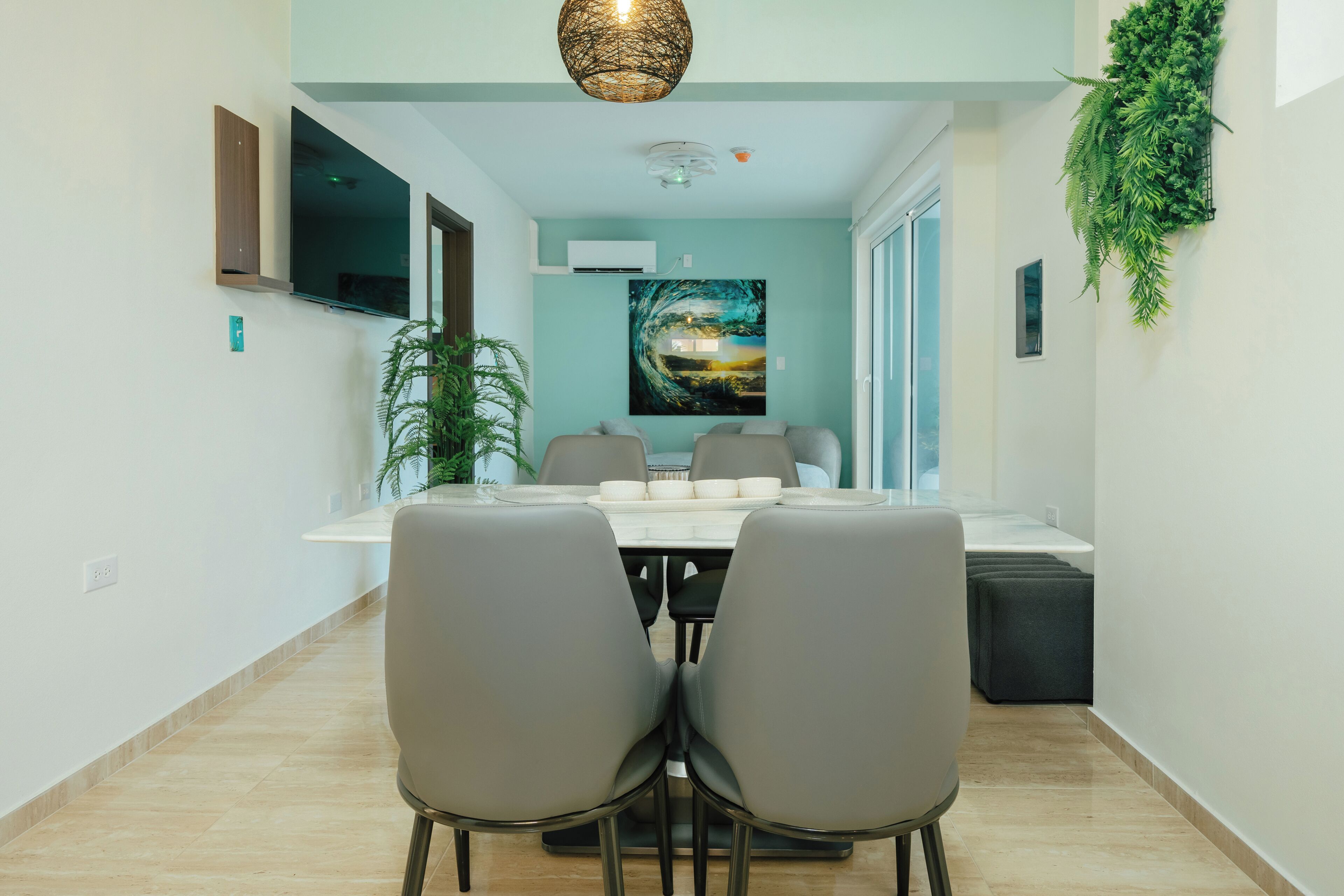 Un espace repas moderne avec une table et des chaises, un téléviseur fixé au mur et un grand tableau accroché au mur.