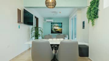 Un espace repas moderne avec une table et des chaises, un téléviseur fixé au mur et un grand tableau accroché au mur.