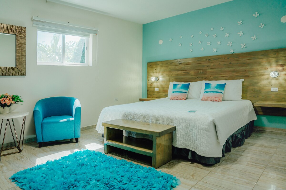 A bedroom with a large bed, a blue chair, a small table, and a blue rug.