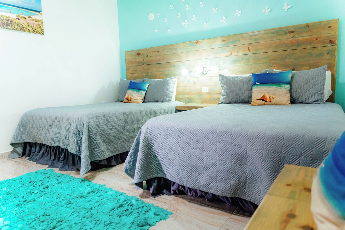 A bedroom with two beds, a wooden headboard, and a teal rug.