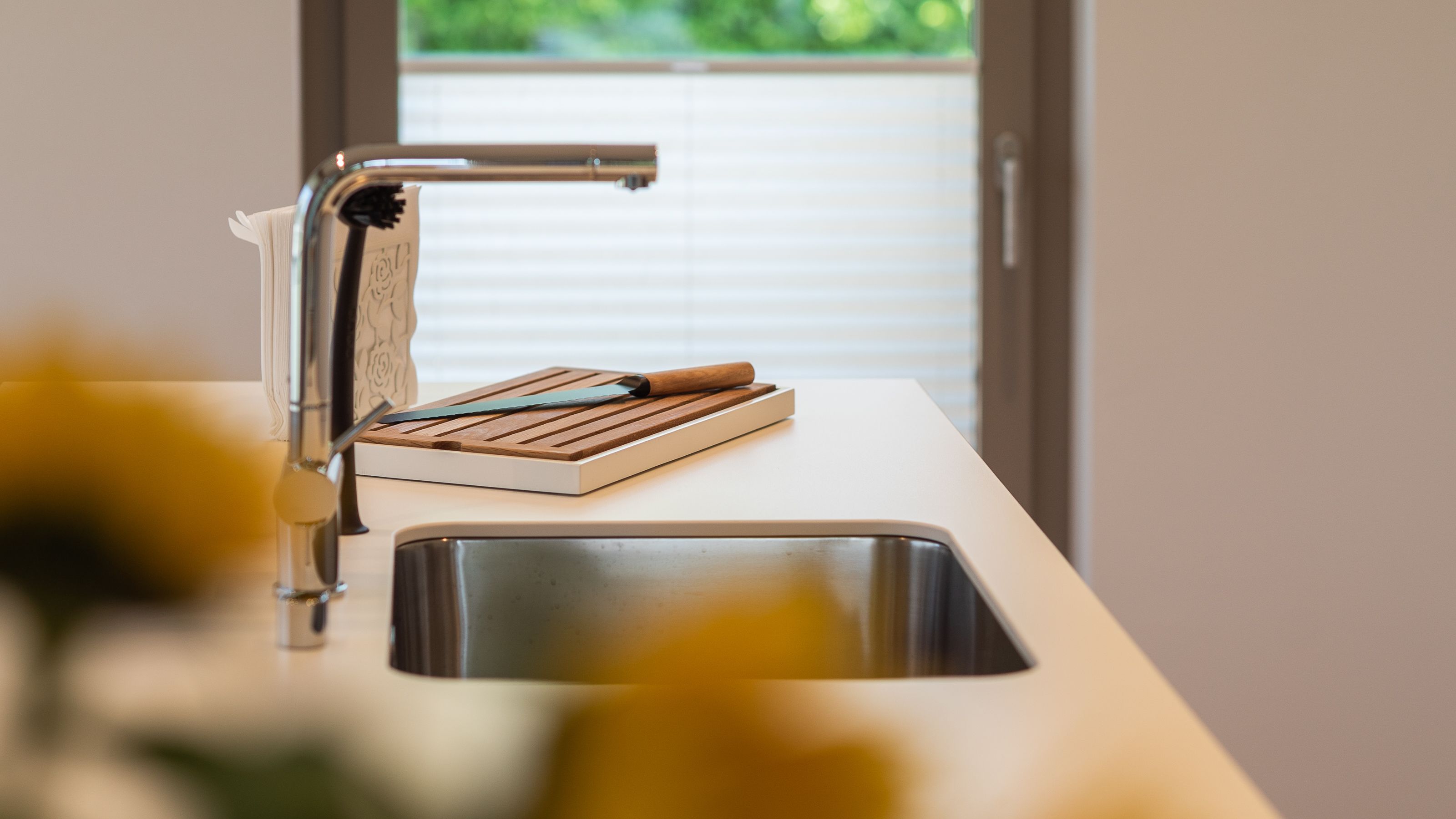 Una cocina moderna con un lavamanos de acero inoxidable, una tabla de cortar de madera y un cuchillo sobre la encimera.