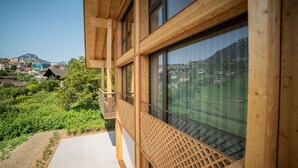 A wooden balcony with large windows overlooking a hillside village. - Seaside Lodge (Spiez)