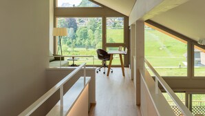 A modern interior with a desk, chair, and a view of a green landscape through large windows. - Seaside Lodge (Spiez)