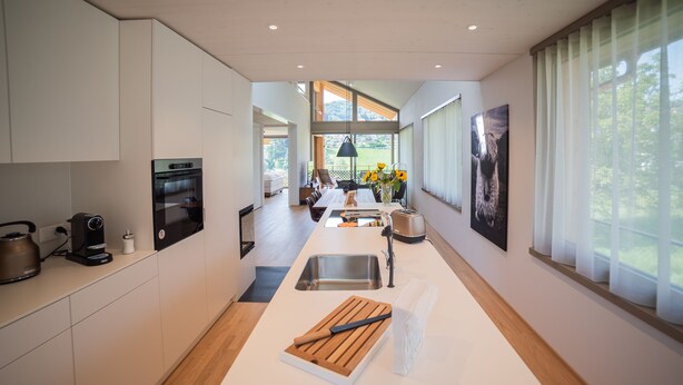 A modern kitchen with built-in appliances, a central island, and large windows offering a view of the outdoors. - Seaside Lodge (Spiez)