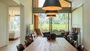 A spacious dining area with a long wooden table, multiple chairs, and a view of a green landscape through large windows. - Seaside Lodge (Spiez)