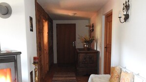 Una sala de estar acogedora con chimenea, suelo de madera, alfombra a rayas, sofá blanco con cojines estampados y un mueble de madera con un jarrón de flores.