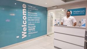 Un comptoir d’accueil avec une pancarte indiquant « Bienvenue » et « Malecon Rooms & Hotel » dans plusieurs langues.