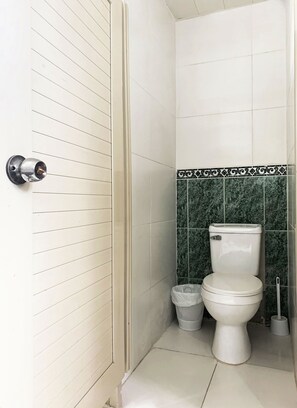 A bathroom with a toilet, a trash bin, and a toilet brush. - Malecon Rooms & Hotel (Santo Domingo)