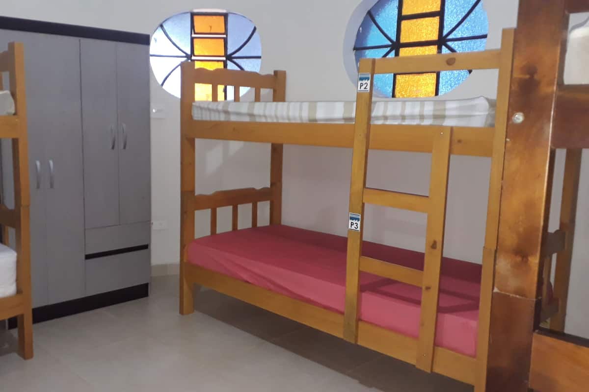 A room with two bunk beds, a wardrobe, and two windows with stained glass.