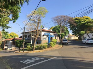 A hostel with a signboard, a tree in front, and a parked car on a sunny street.