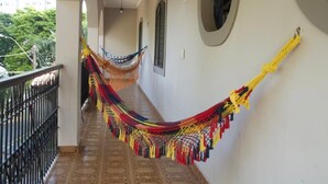 Un pasillo con una hamaca colgada en la pared, un balcón con barandilla y un edificio al fondo.