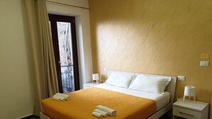 A hotel room with a bed, two bedside tables, a window with curtains, and a view of the outside. - Giò Rooms (Scalea)