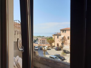 Vista desde una ventana sobre una calle costera con coches aparcados y edificios.
