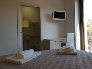 A hotel room with a bed, a desk, a TV, and a bathroom visible through an open door. - Giò Rooms (Scalea)