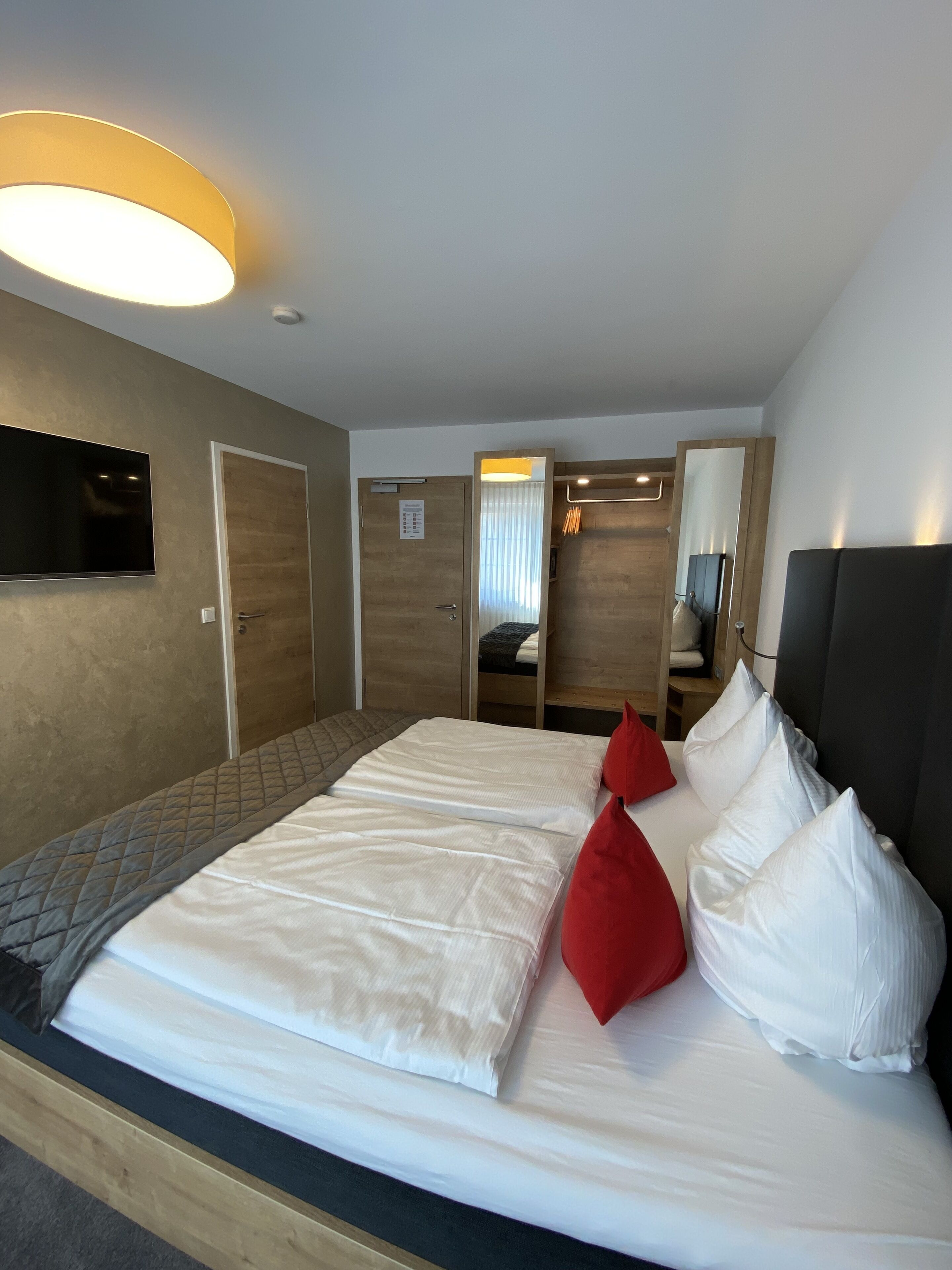 A hotel room with a large bed, a flat-screen TV mounted on the wall, a wooden door, and a mirror.