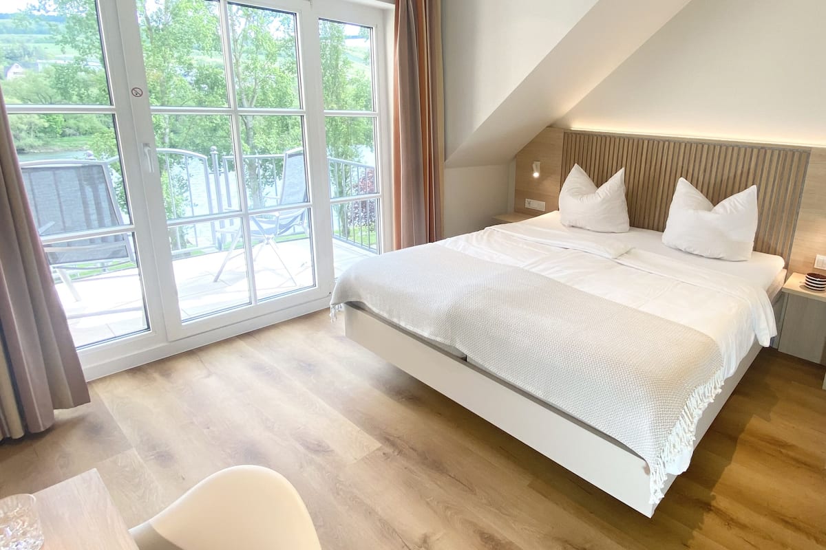 A bedroom with a large bed, a desk, and a view of the outdoors through a sliding glass door.