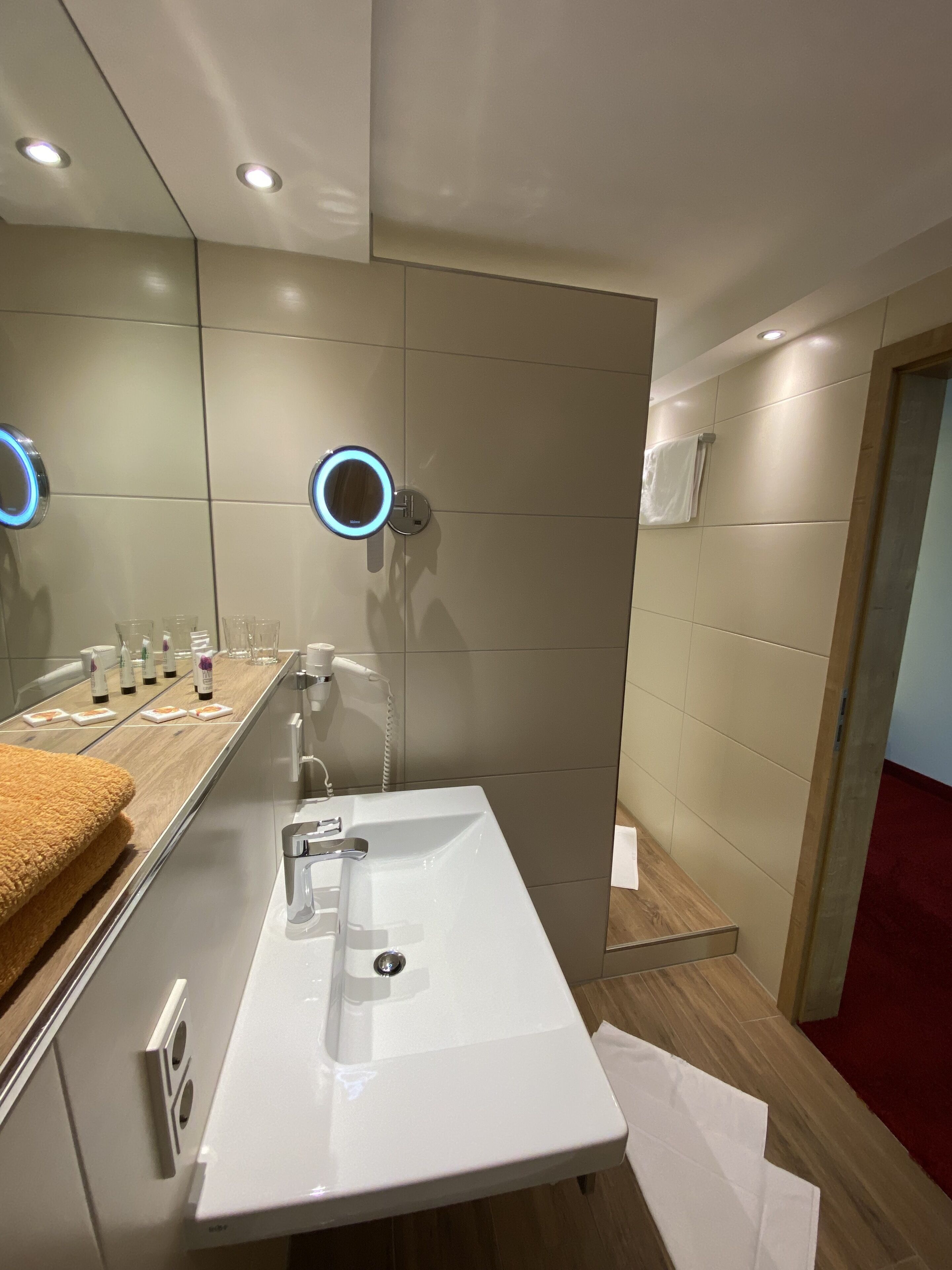 Un baño moderno con un lavabo blanco, un espejo con luz circular y artículos de aseo en la encimera.