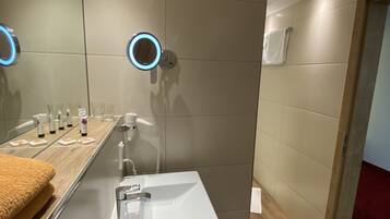 Un baño moderno con un lavabo blanco, un espejo con luz circular y artículos de aseo en la encimera.