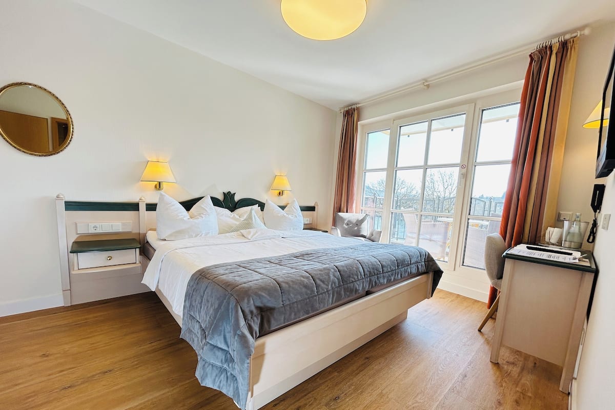 A hotel room with a large bed, bedside tables, a desk, and a window with curtains.