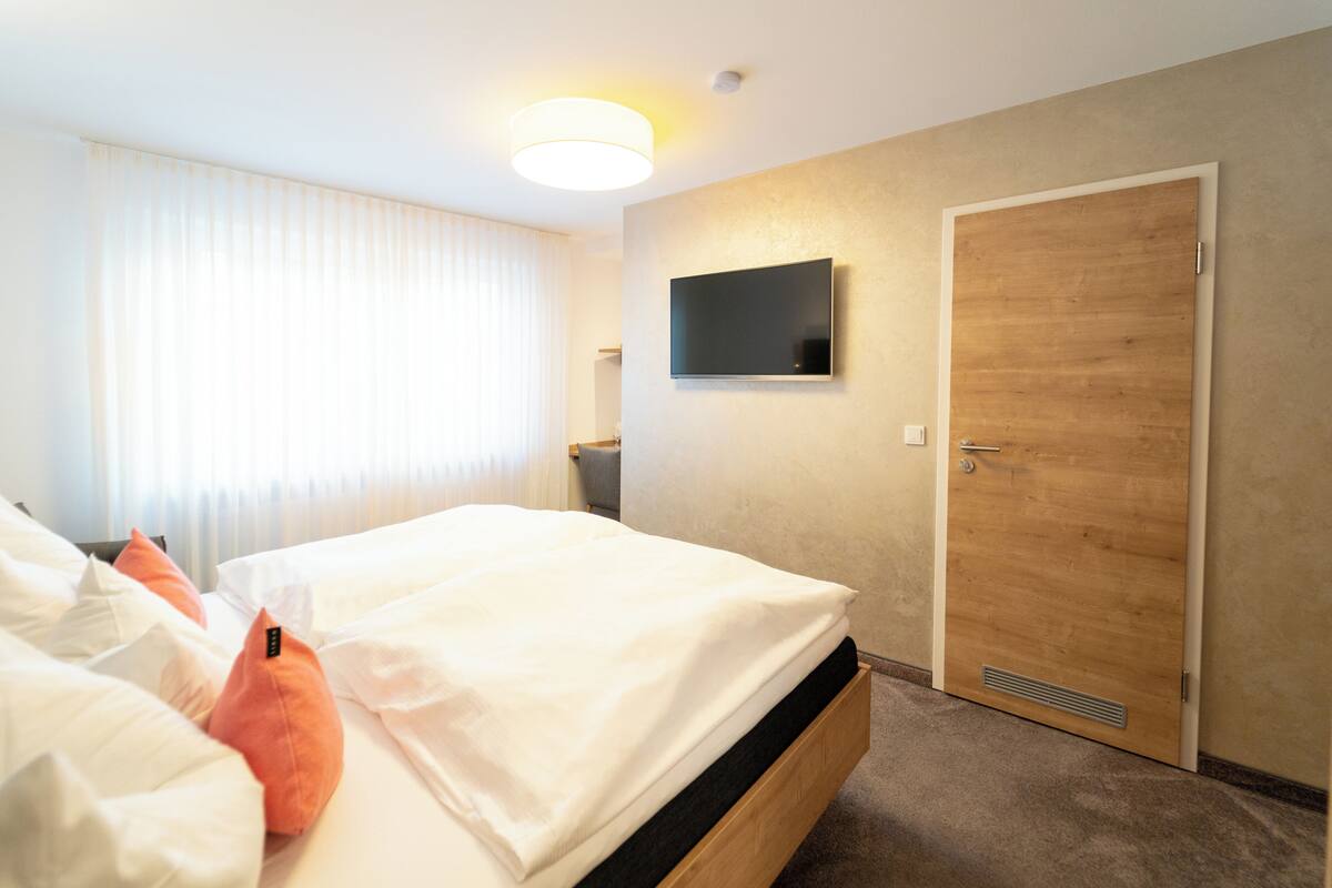 A hotel room with two beds, a TV mounted on the wall, and a wooden door.