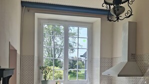 Une cuisine avec une fenêtre, un évier, une cuisinière et un luminaire suspendu.