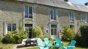 Un bâtiment en pierre doté de nombreuses fenêtres, un jardin avec des chaises et une table.