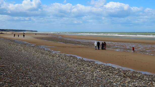 Une plage de galets où l’on voit des gens se promener le long du rivage.