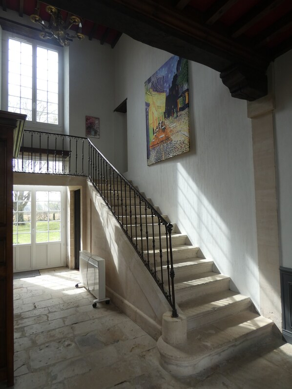 A staircase with a black railing leading to a second floor, a large painting on the wall, and a view of the outside through a window. - Charming house in a quiet (BARBEVILLE)