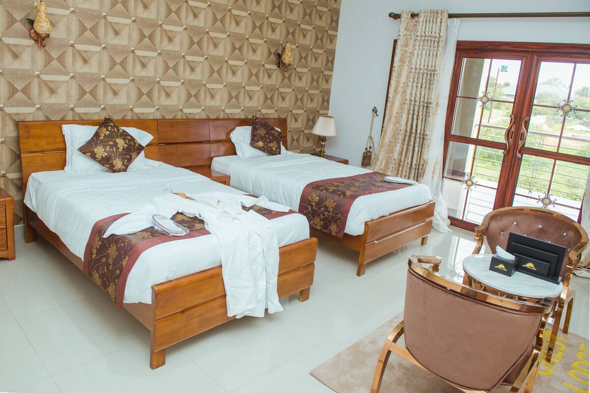 A hotel room with two wooden beds, a brown leather armchair, and a large window with a view.