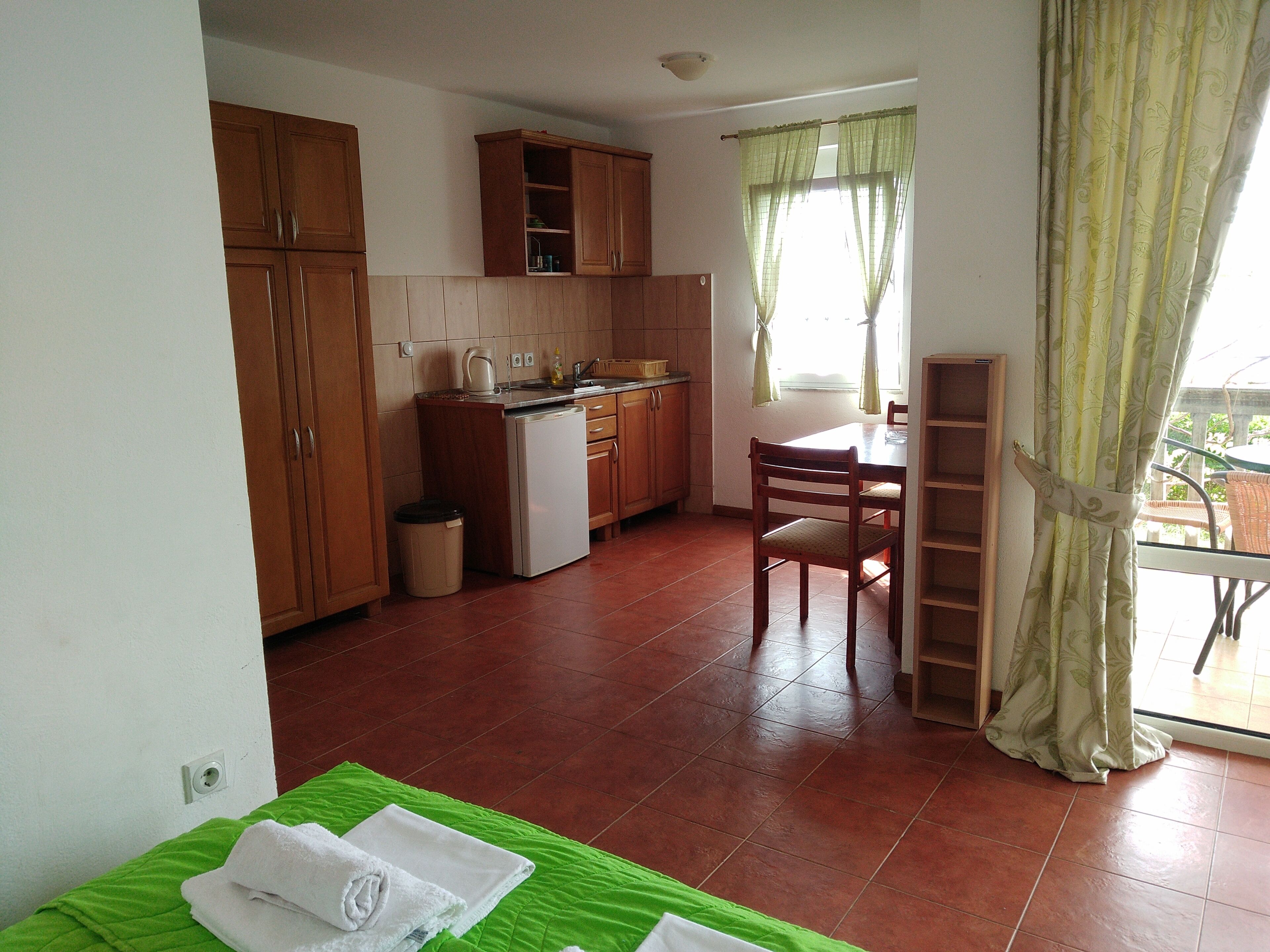 Una cucina compatta con mobili in legno, un piccolo frigorifero e una zona pranzo con tavolo e sedie.