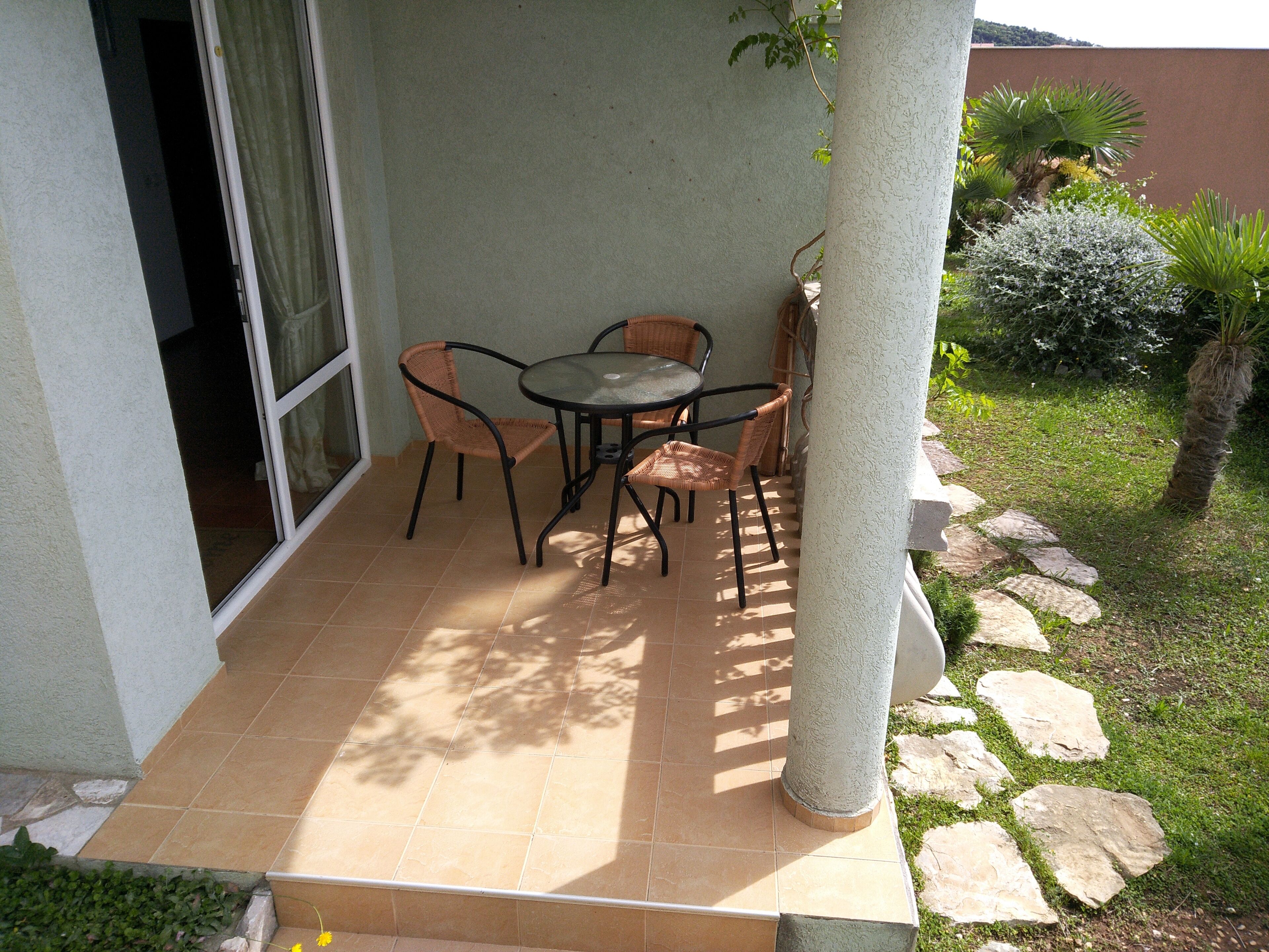 An outdoor patio with a table and chairs, a stone pathway, and a small garden area.