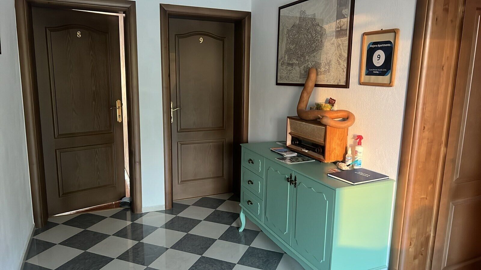 Ein Flur mit zwei Holztüren, einem türkisfarbenen Schrank mit Radio und einem gerahmten Zertifikat an der Wand.