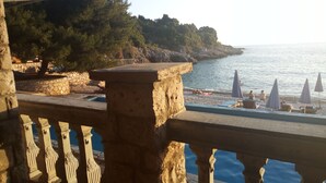 A stone balustrade overlooking a beach with umbrellas and a pool. - Majero Apartments (Utjeha)