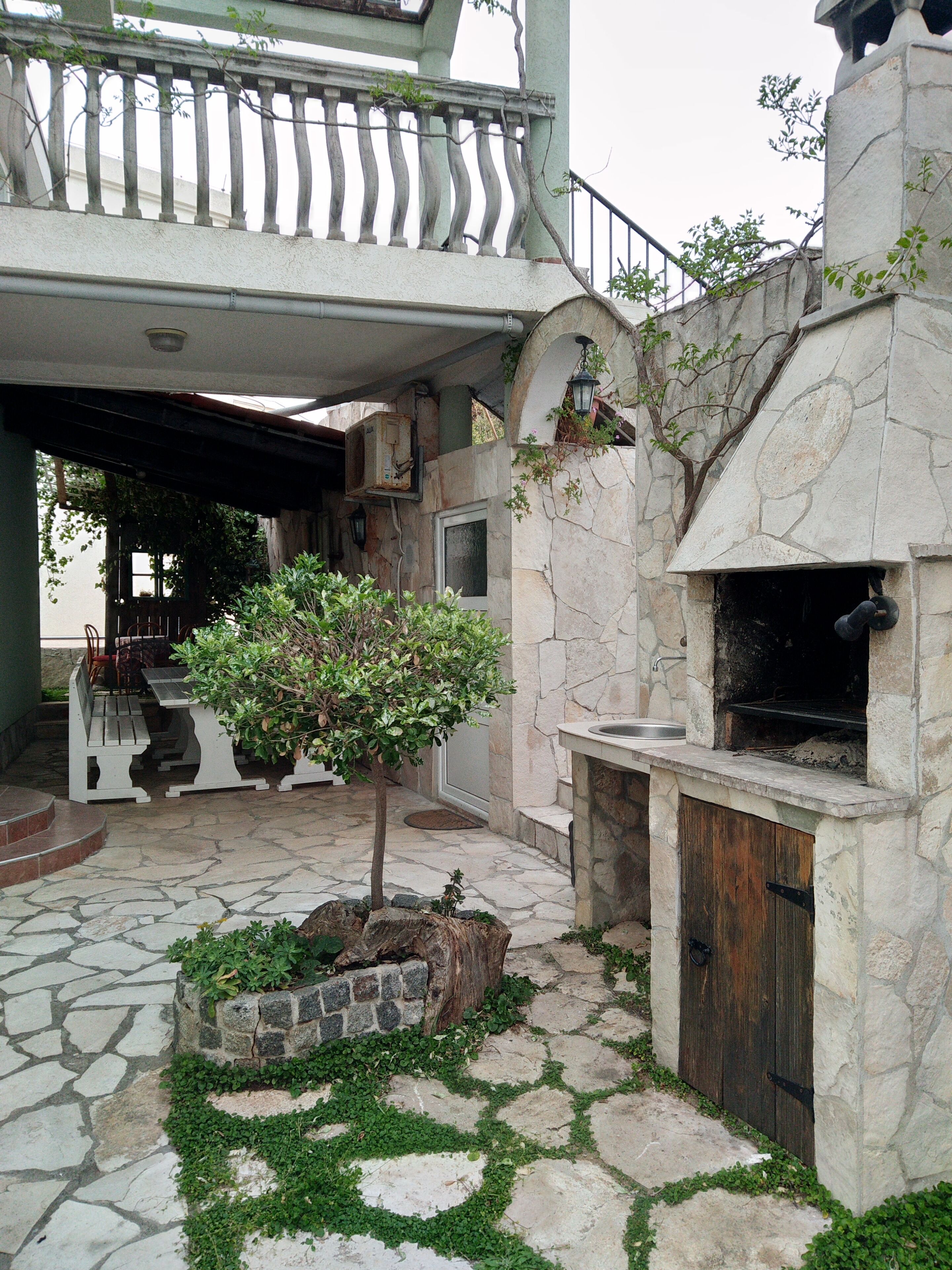 A stone patio with a small tree, a stone fireplace, and a wooden door.