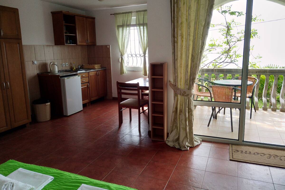 A compact kitchen with a dining area, a small refrigerator, and a window with curtains.