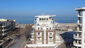 Un edificio de varios pisos con balcones, vistas despejadas al mar y un estacionamiento al frente.