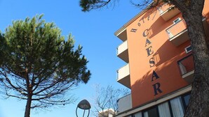 Un edificio con el letrero "HOTEL CAESAR" en su fachada, rodeado de árboles y un cielo despejado.
