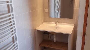 Un baño con lavamanos blanco, espejo y ducha. Hay una alfombra roja en el suelo.