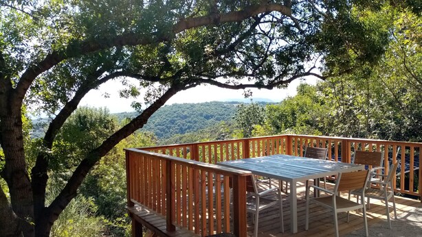 Eine Holzterrasse mit Tisch und Stühlen mit Blick auf ein bewaldetes Tal.