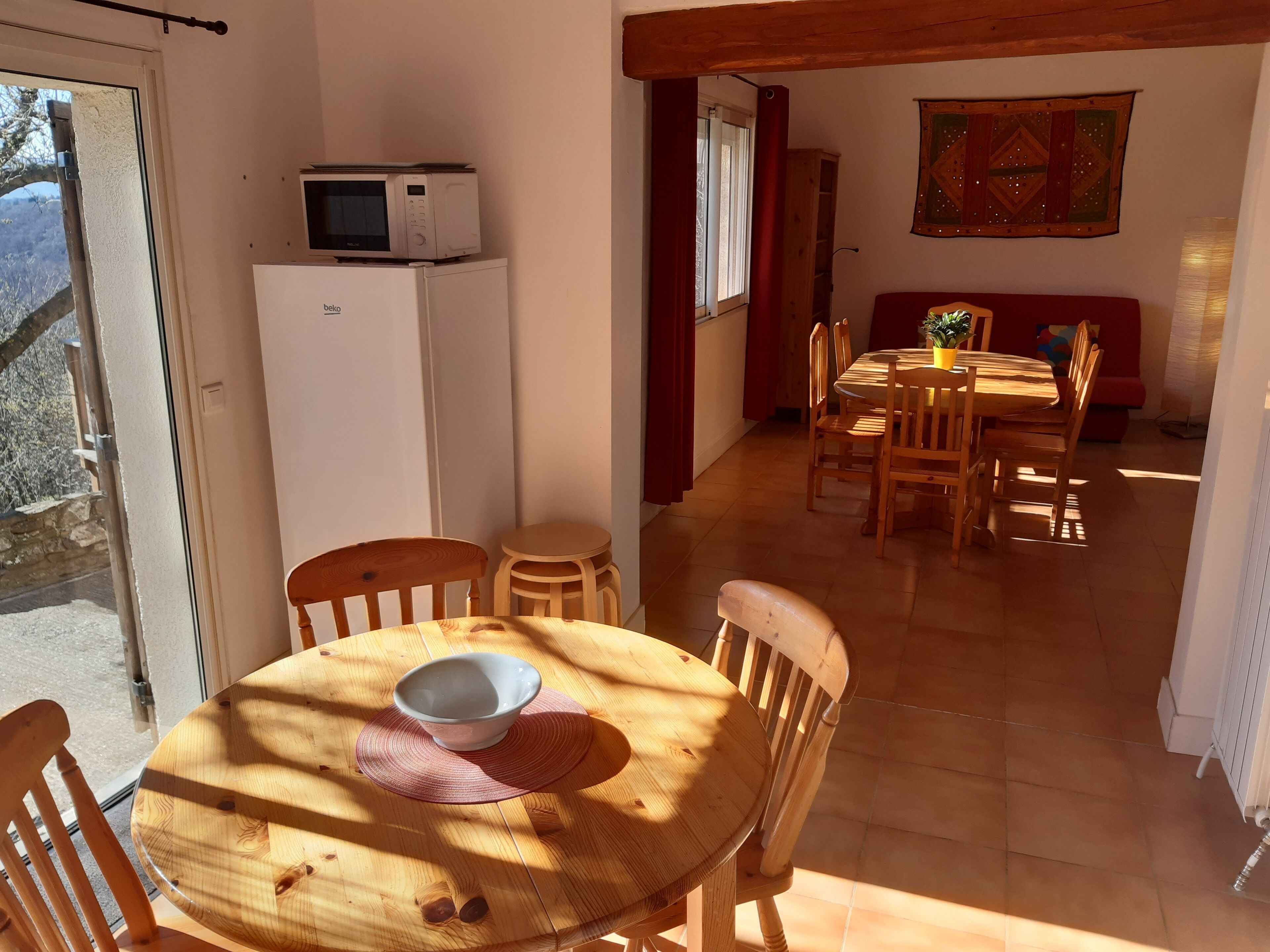 A dining area with a round wooden table, chairs, a white refrigerator, and a microwave on top.