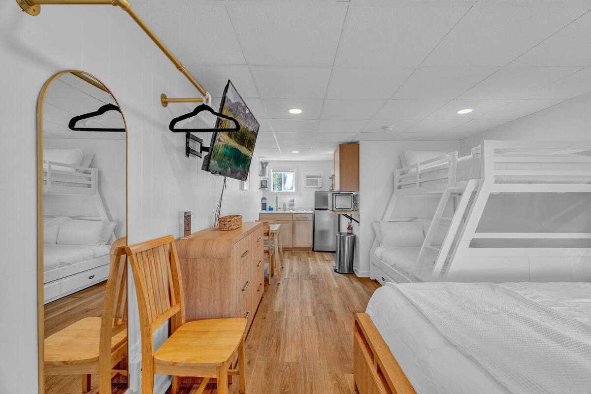 Une chambre d’hôtel compacte avec des lits superposés, une commode en bois, une petite table et un coin cuisine.