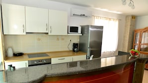 Una cocina con armarios blancos, un refrigerador de acero inoxidable, un microondas, una cafetera y un lavamanos.