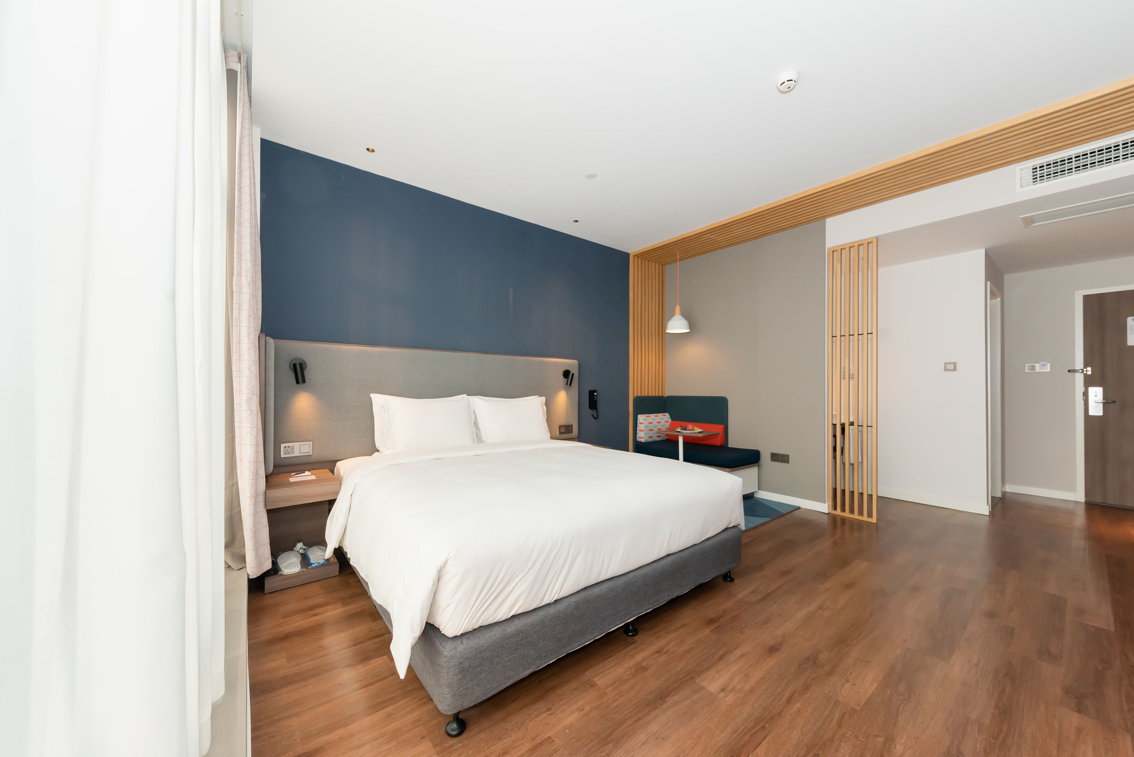 A modern bedroom with a large bed, bedside tables, a nightstand, and a wall-mounted lamp.