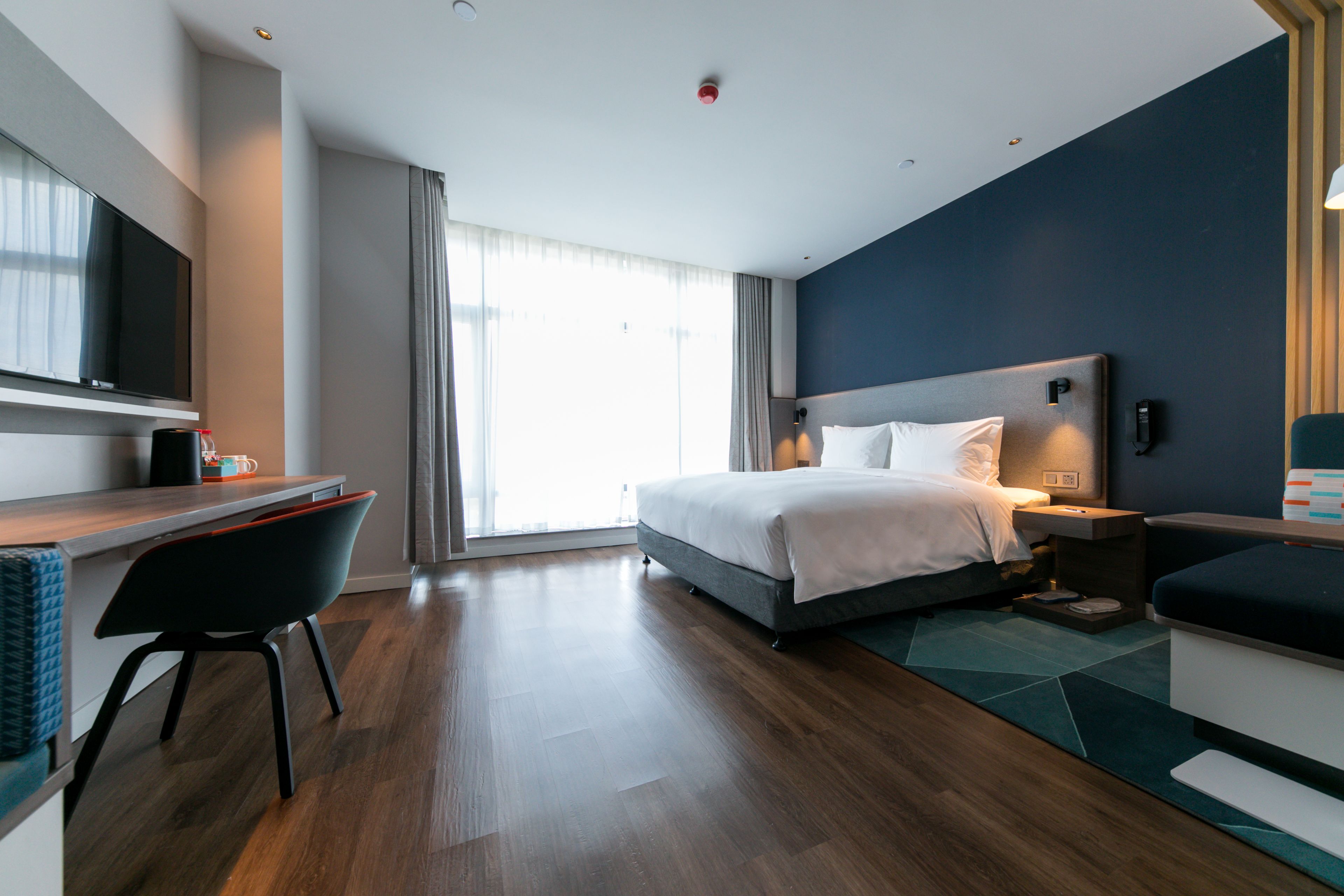 A modern hotel room with a bed, desk, chair, and a TV.