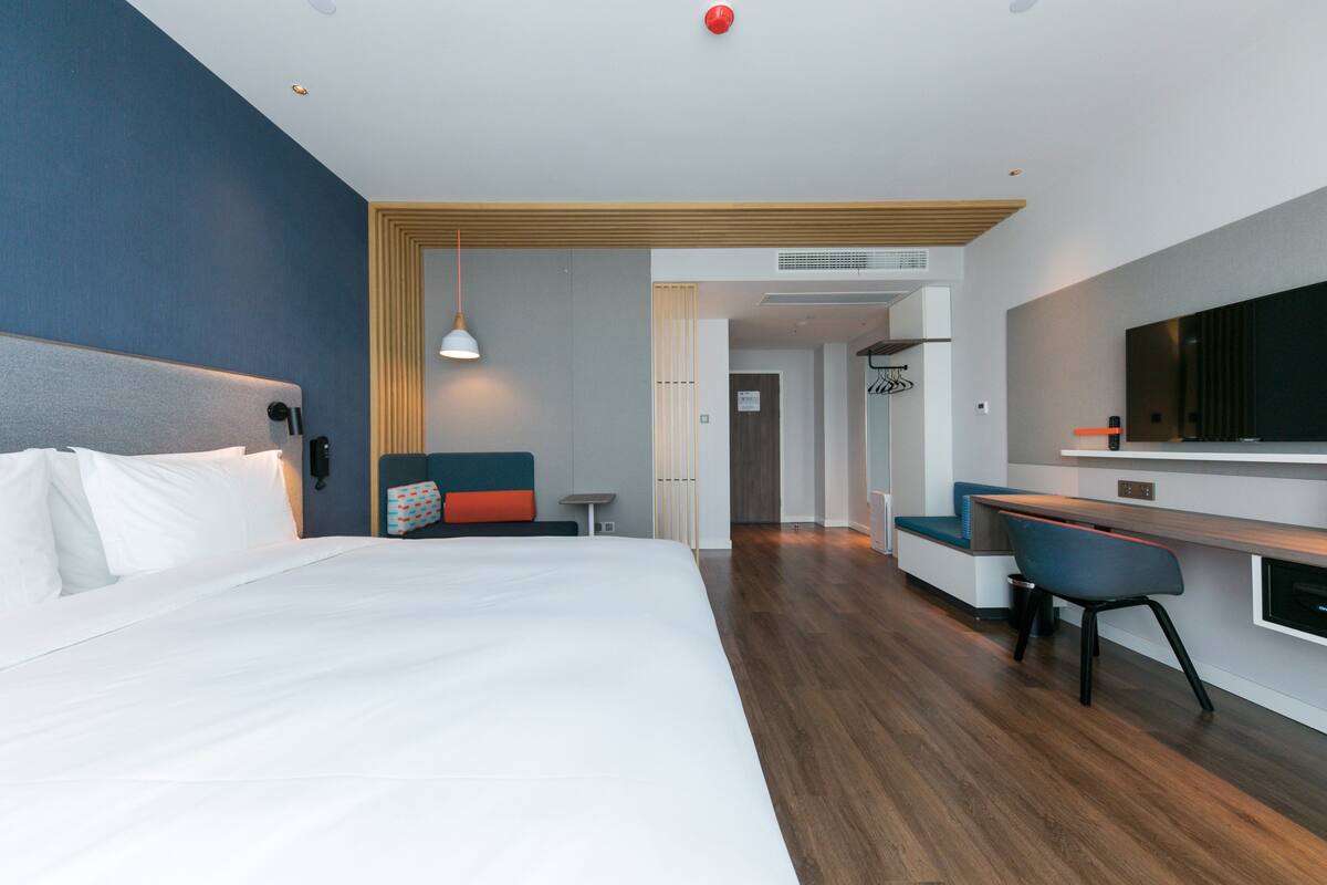 A modern hotel room with a large bed, a desk, and a seating area.